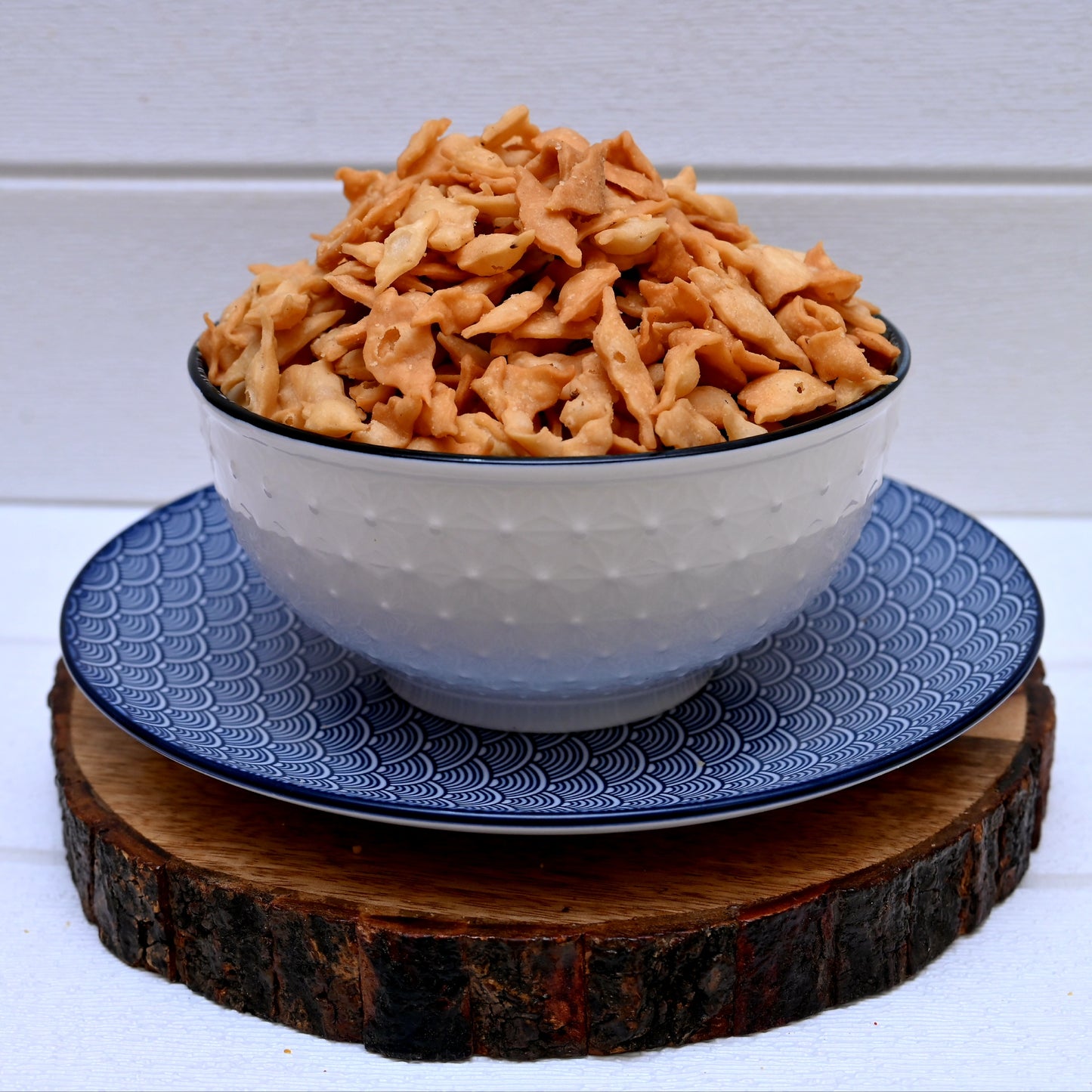 Bowl of nimki (shakarpara) on a blue plate with a wooden coaster underneath