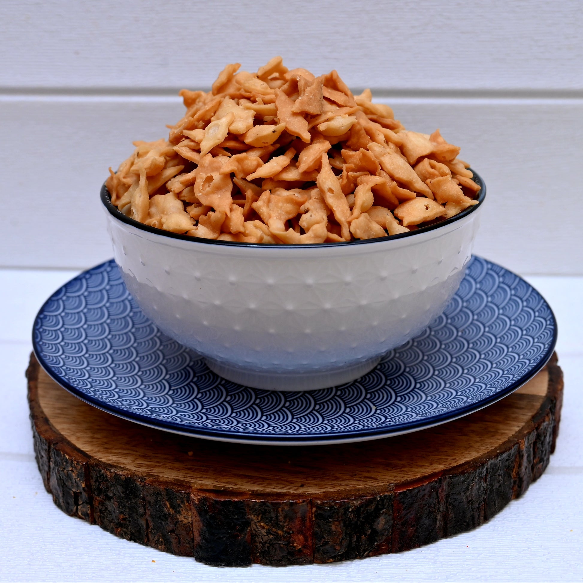 Bowl of nimki (shakarpara) on a blue plate with a wooden coaster underneath
