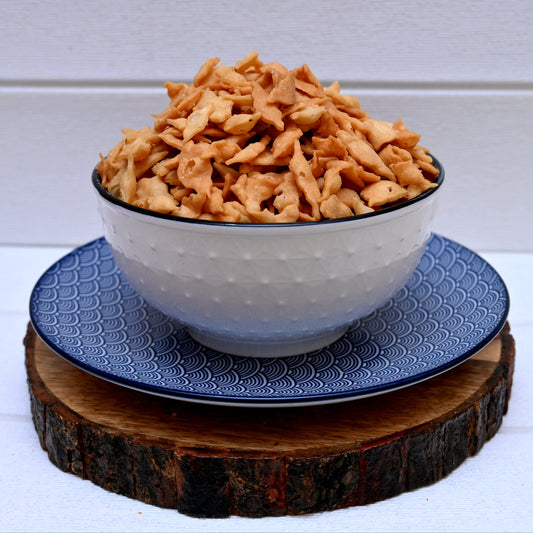 Bowl of nimki (shakarpara) on a blue plate with a wooden coaster underneath